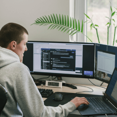 Man in grey hoodie working with multiple computer screens